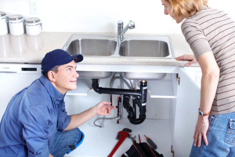 Plumber repairing kitchen sink plumbing for a homeowner
